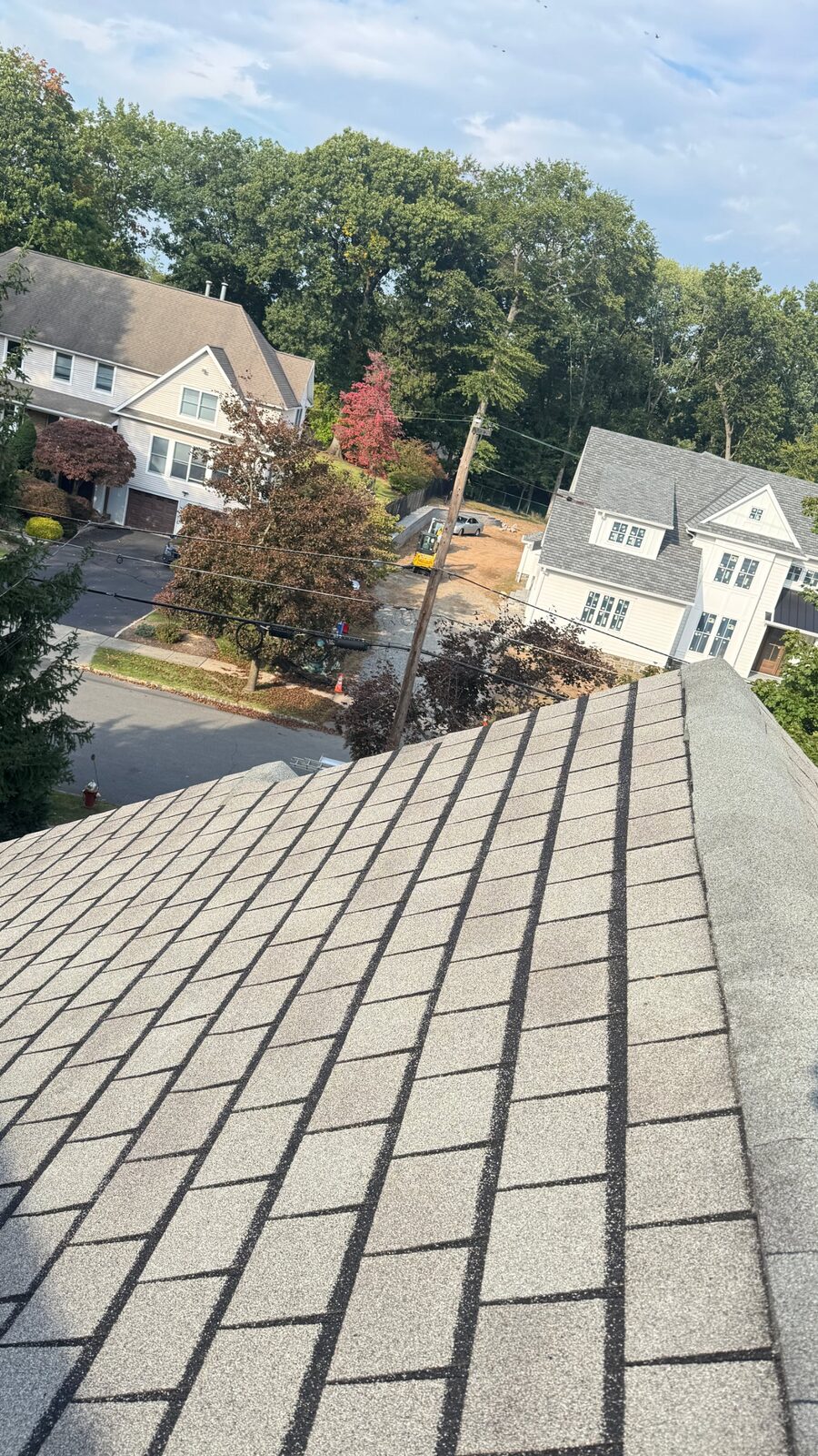Gray weathered shingle roof on a Mountain Lakes, NJ home before repair, looking down the slope at a residential neighborhood with mature trees and mixed housing